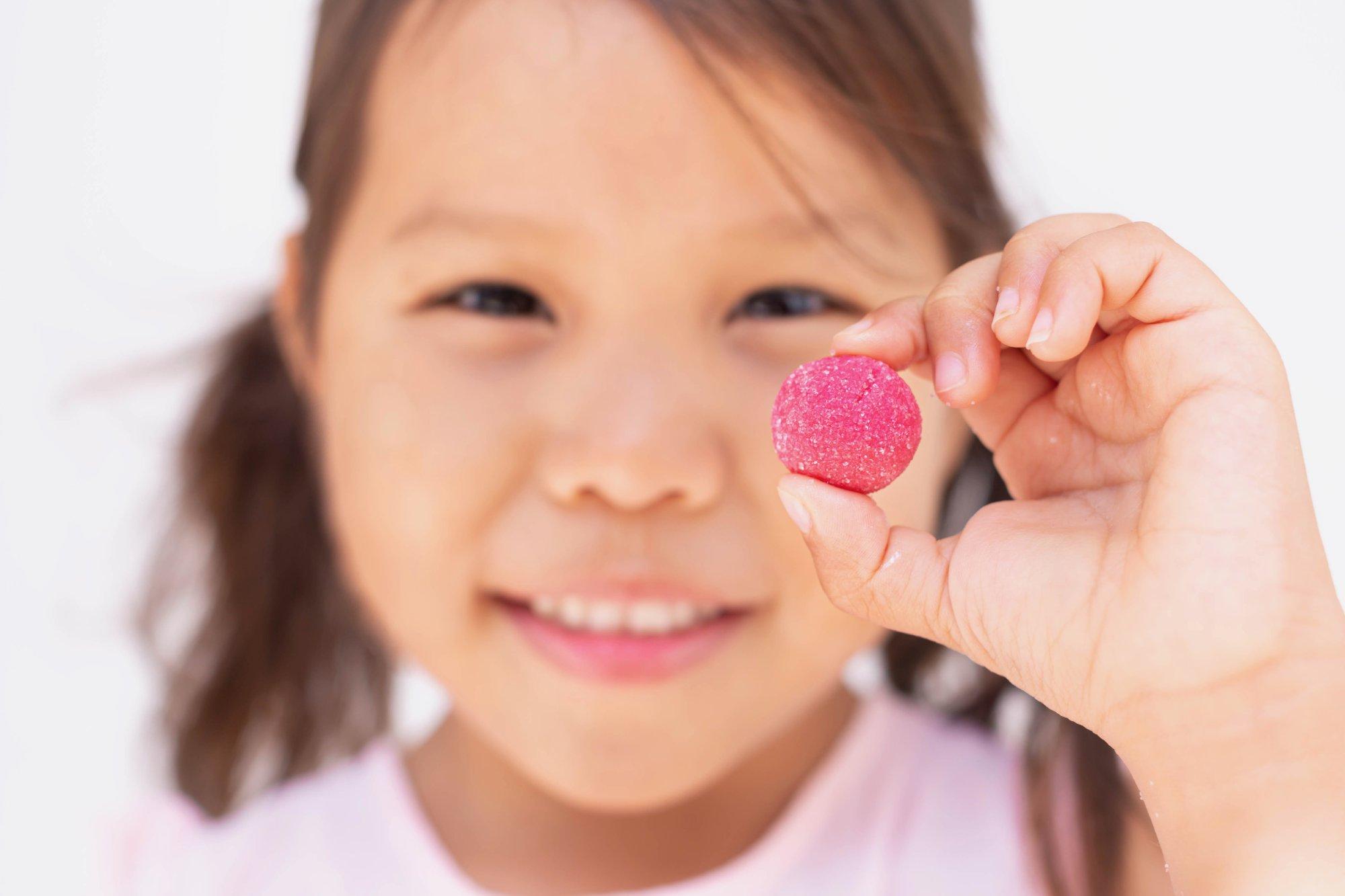 A little girl holding up a sugar candy vitamin. Children supplement