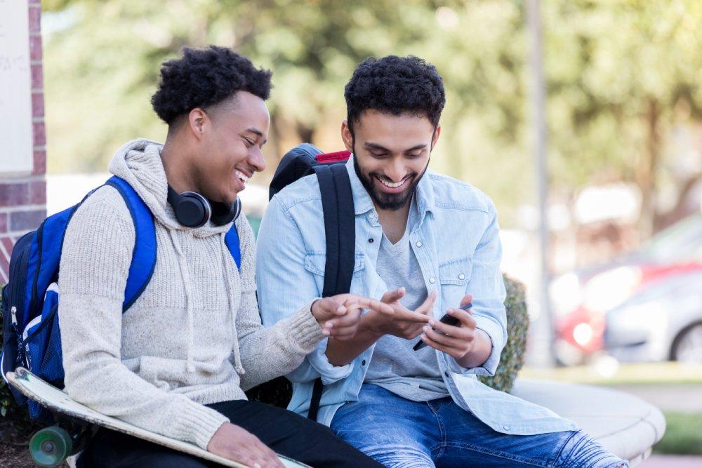 Cheerful_male_college_students_look_at_smartphone