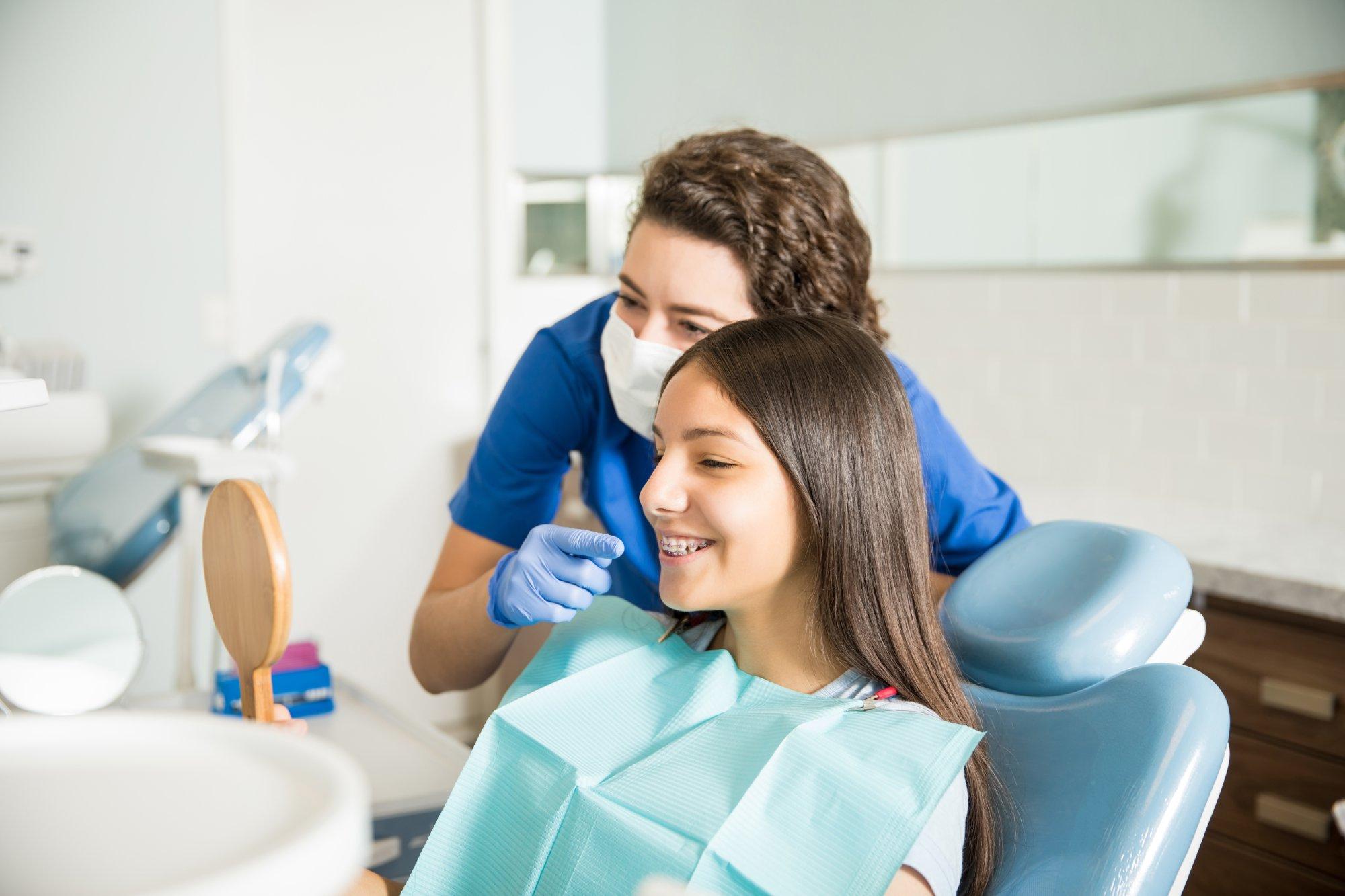 Dentist Showing Braces To Teenage Girl In Mirror At Clinic