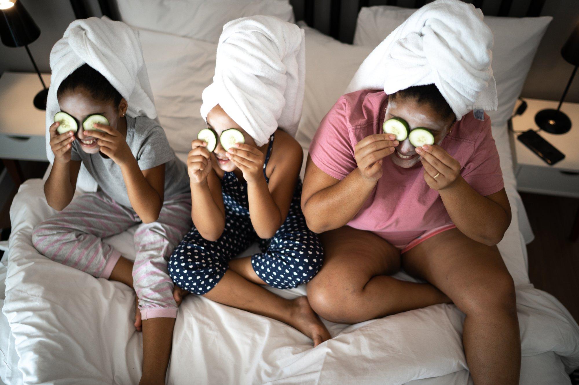 Morther and daughters in bed doing skin care with cucumber slices over the eyes