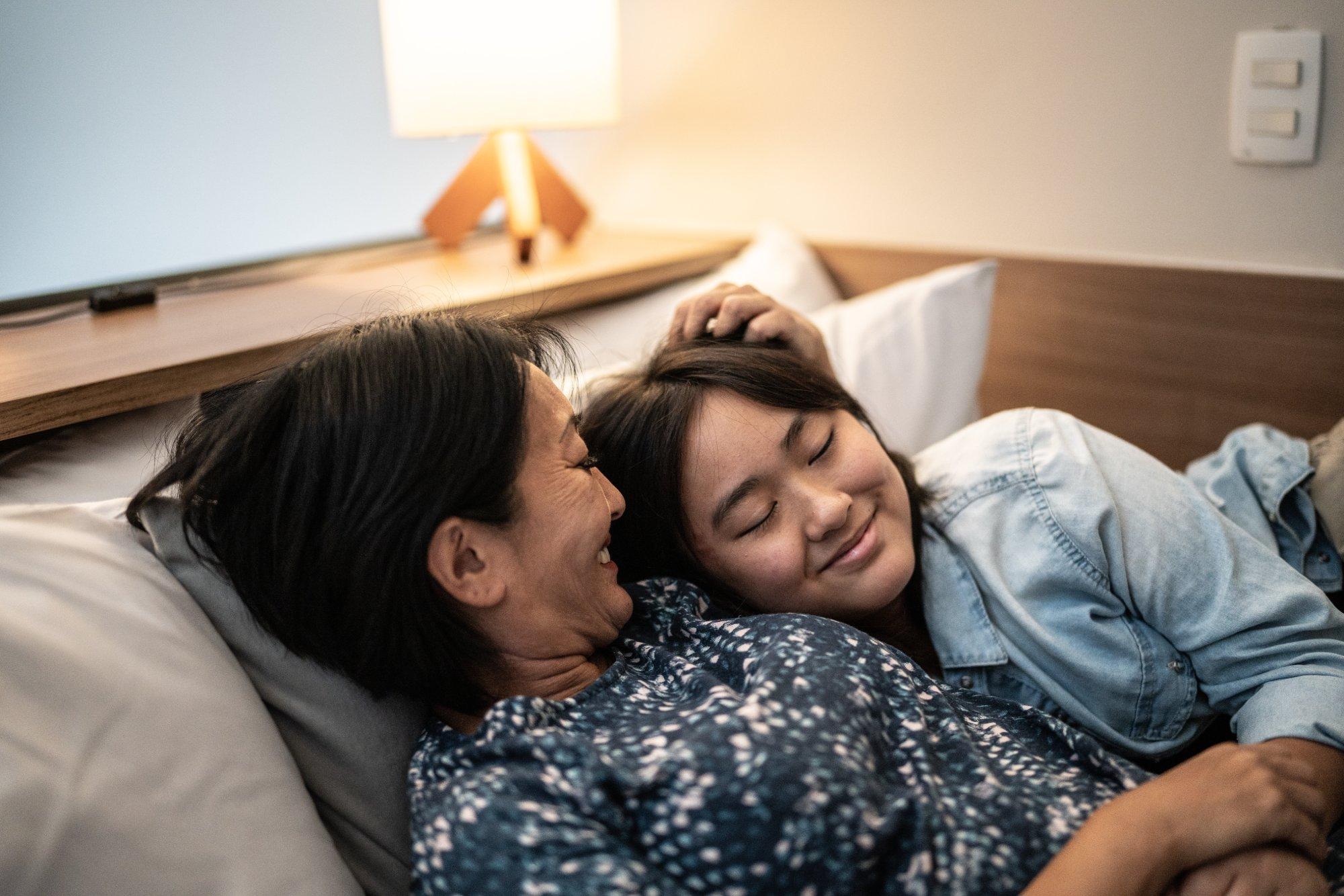 Mother laying down with daughter in bed at home