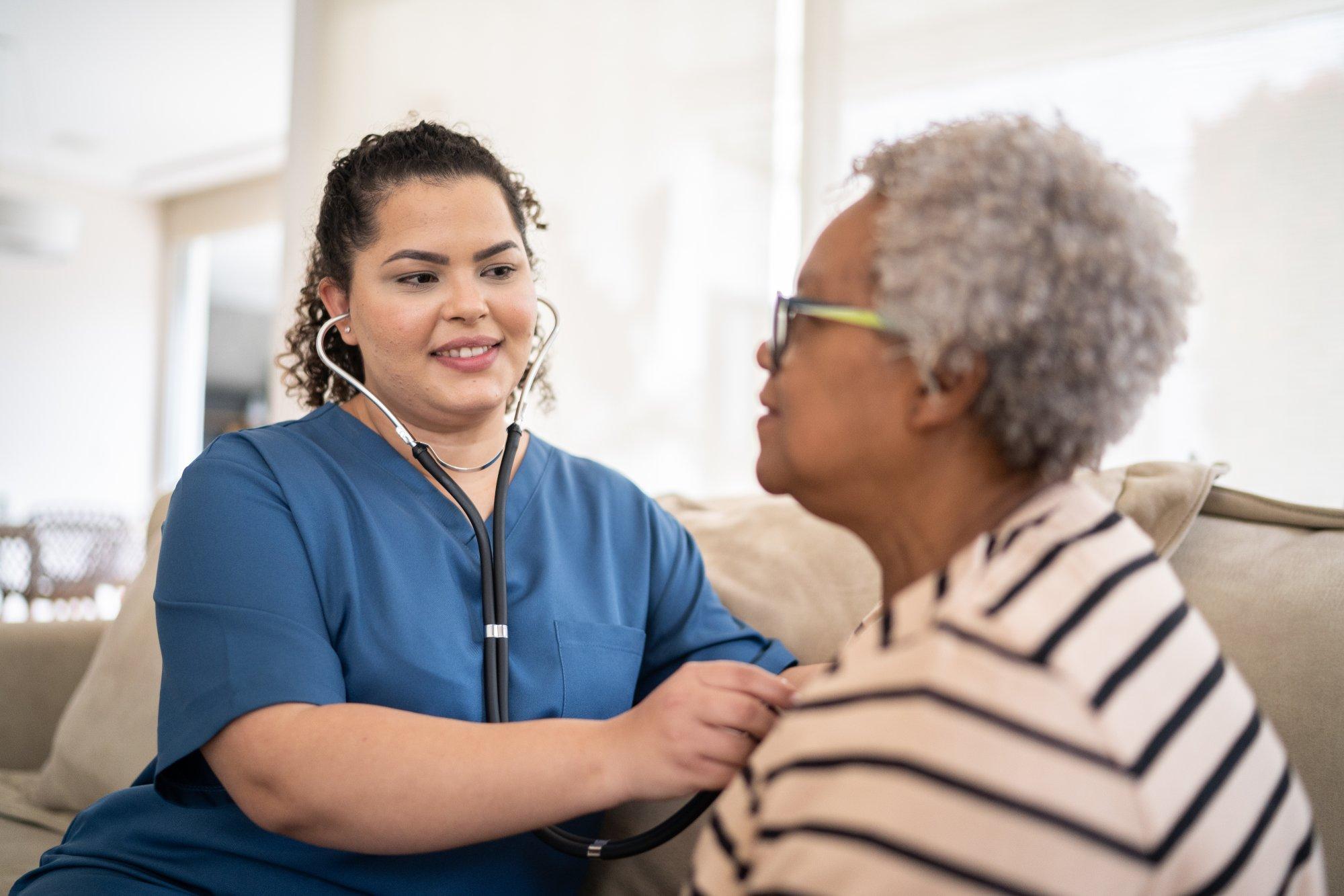 Nurse listening to senior patient's heartbeat during home visit