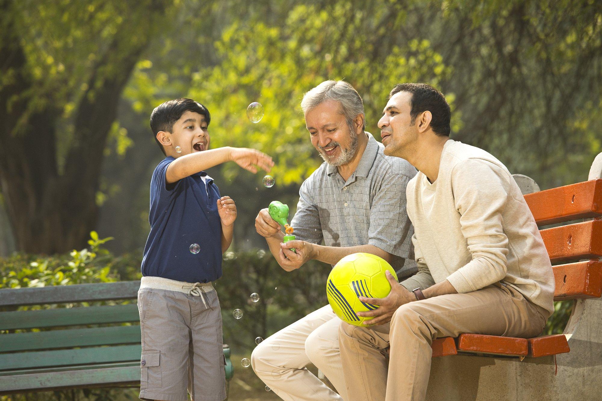 Senior man blowing bubbles with son and grandson at park