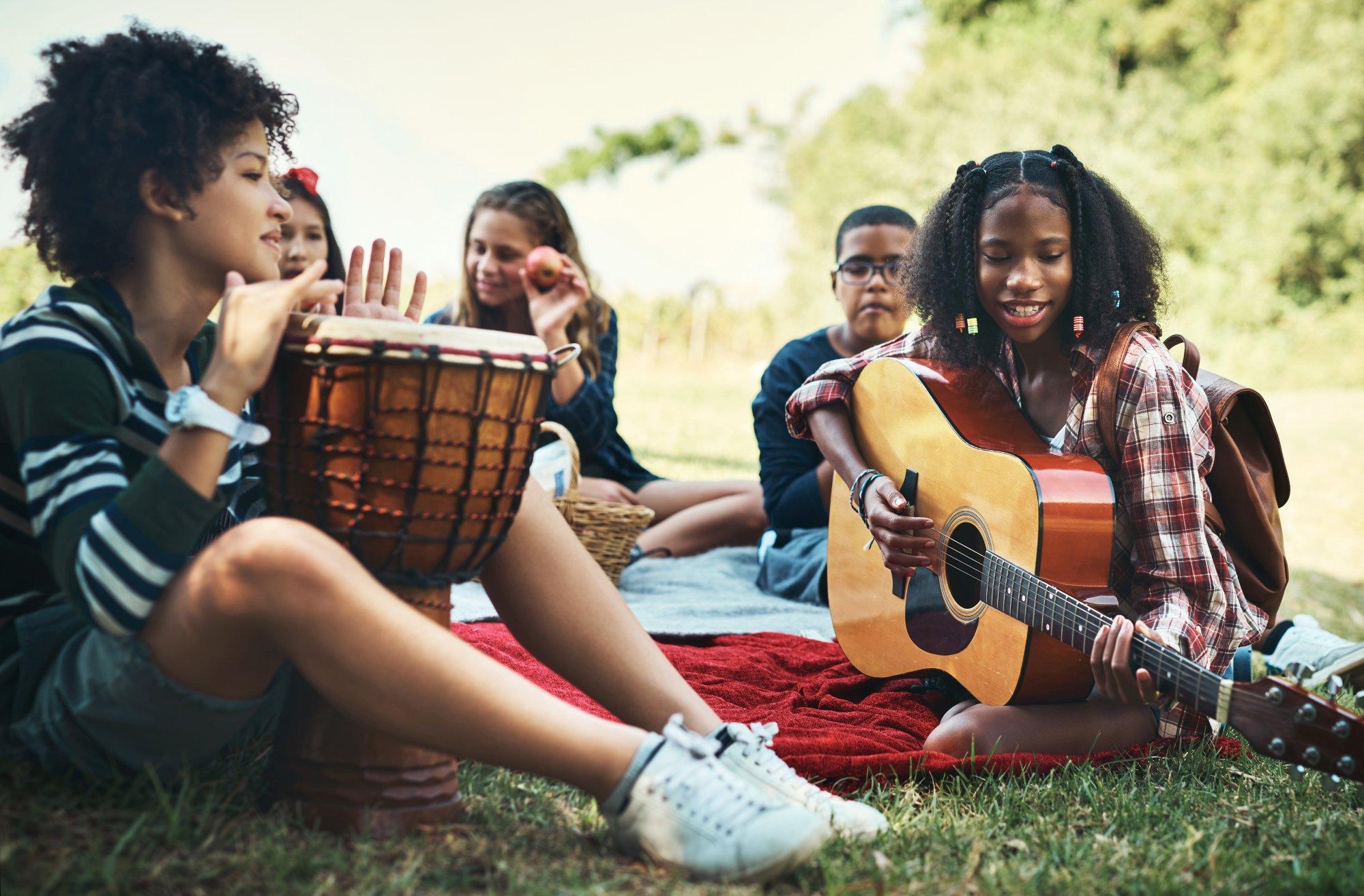 Shot of a group of teenagers playing musical instruments in nature at summer camp