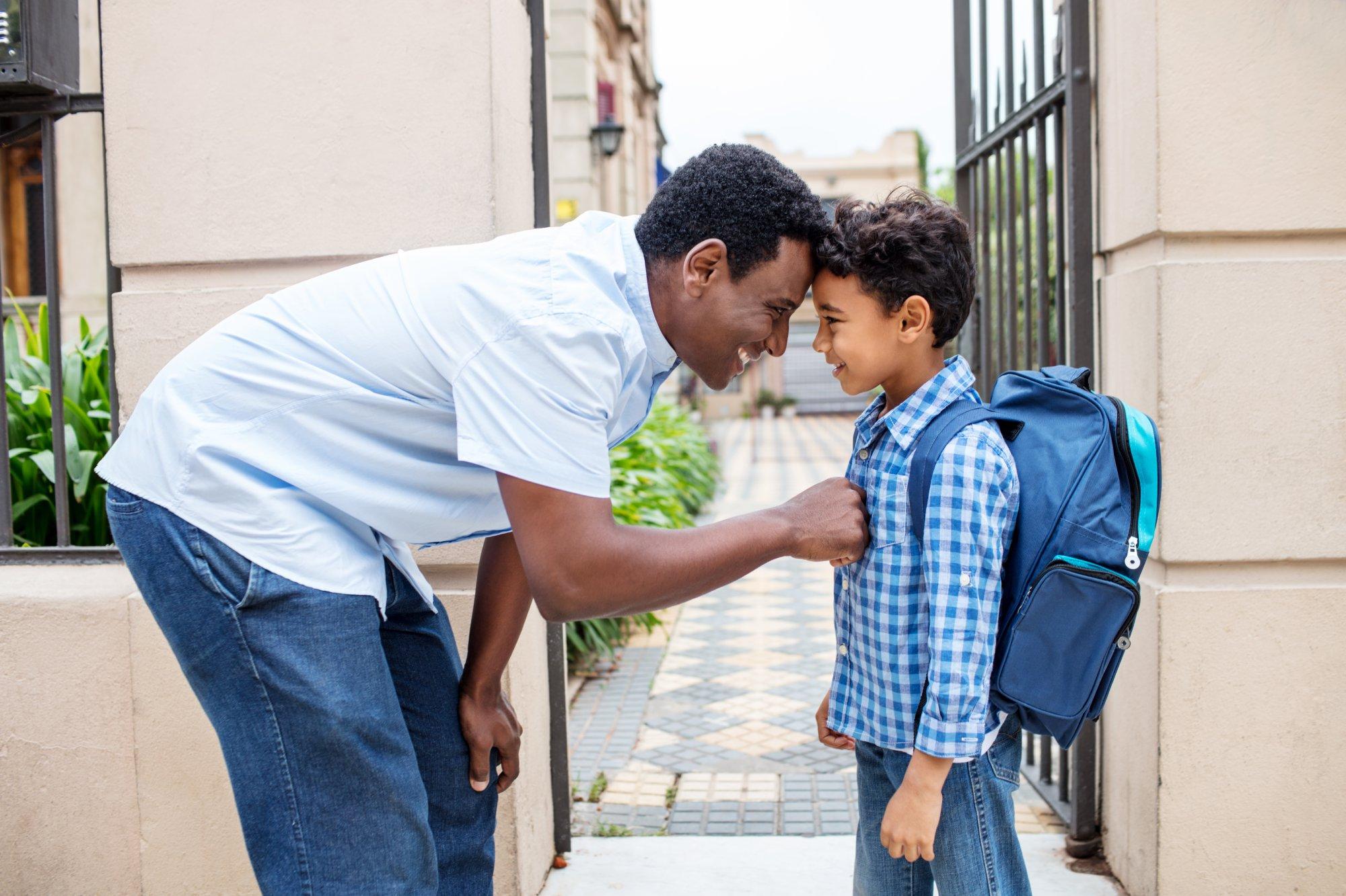 Smiling father leaving son with backpack to school