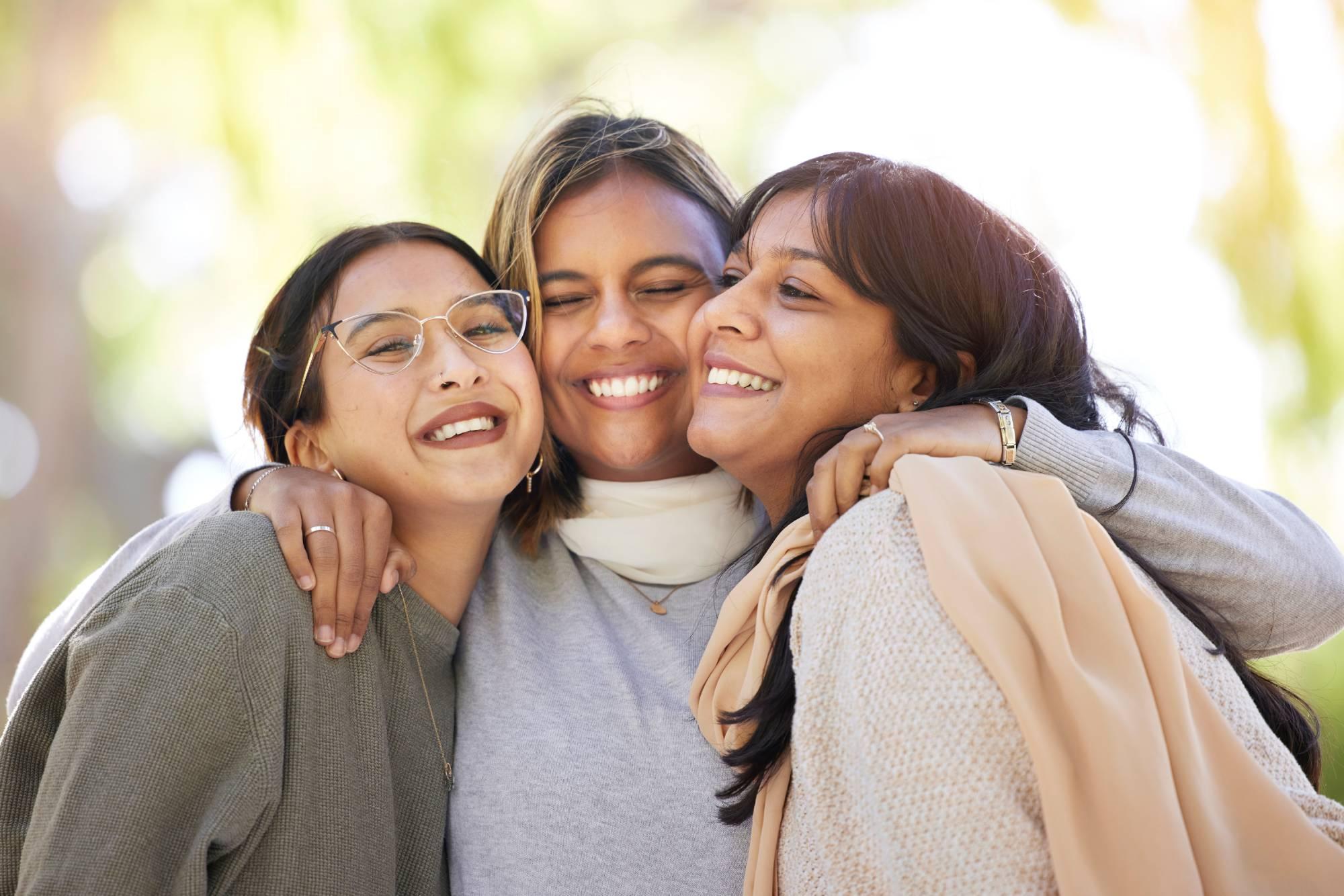 Women friends, hug and smile in park for happiness, support and relax in sunshine at best friends reunion. Woman group, happy and love embrace with care, nature and blurred background in Los